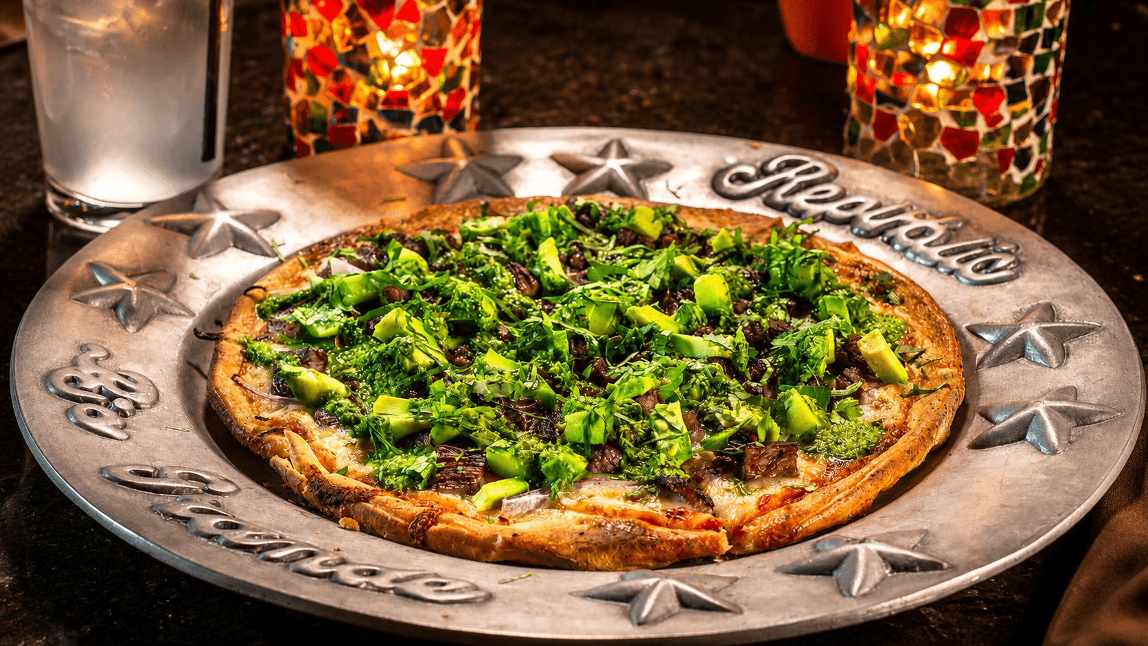 Specialty brick-oven pizza with avocado and greens
